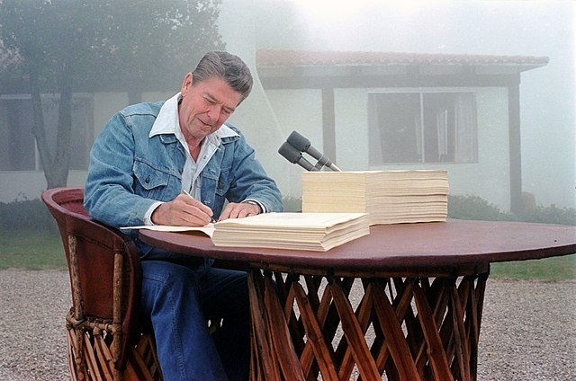 President Ronald Reagan signing the Economic Recovery Tax Act of 1981 and the Omnibus Budget Reconciliation Act of 1981 at his Santa Barbara, California ranch, Rancho del Cielo, 13 August 1981. Photograph by official White House photographer, Karl Schumacher, courtesy of the Ronald Reagan Presidential Library (C03490-4A, https://www.reaganlibrary.gov/archives/photo/c03490-01).