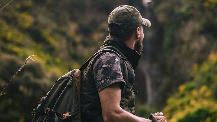 man wearing cap and crew neck shirt standing in the middle of forest