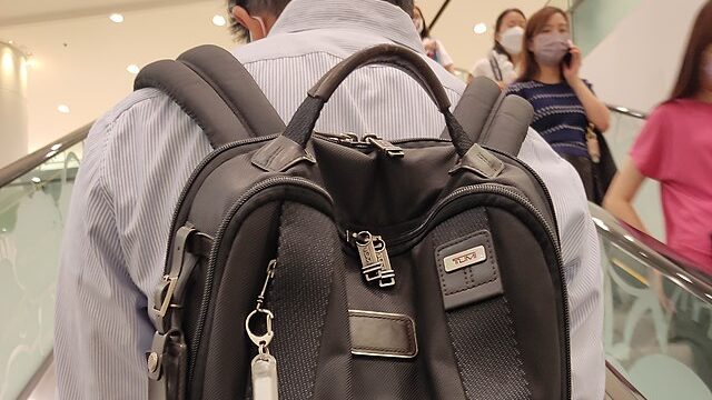 Tumi laptop backpack on man in wrinkled shirt going up an escalator